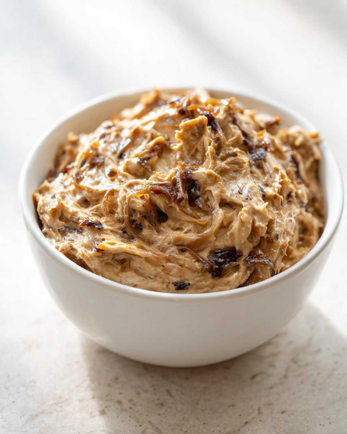 Close-up of creamy caramelized onion dip topped with dark, sweet caramelized onions in a white bowl.