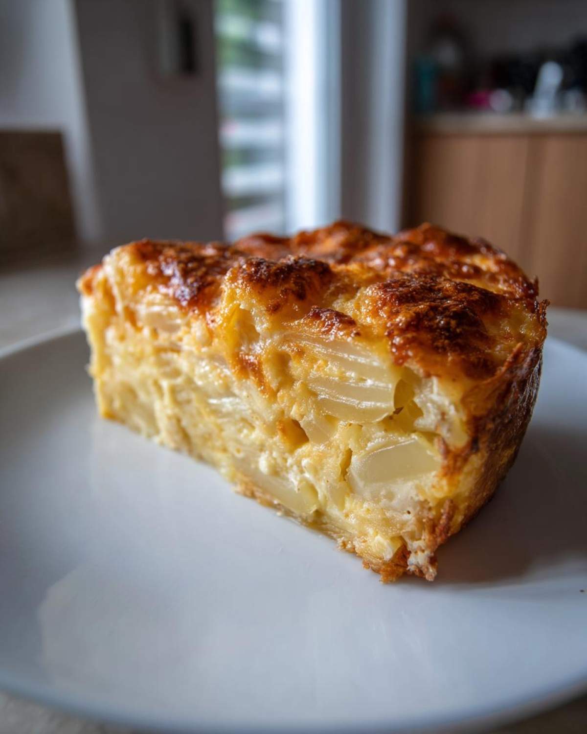 A thick slice of creamy cheesy scalloped potatoes with a golden-brown, bubbly top, served on a white plate.