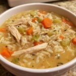 Close-up of a creamy chicken and rice soup featuring shredded chicken, diced carrots, and celery, perfect for a comforting wild rice soup recipe.