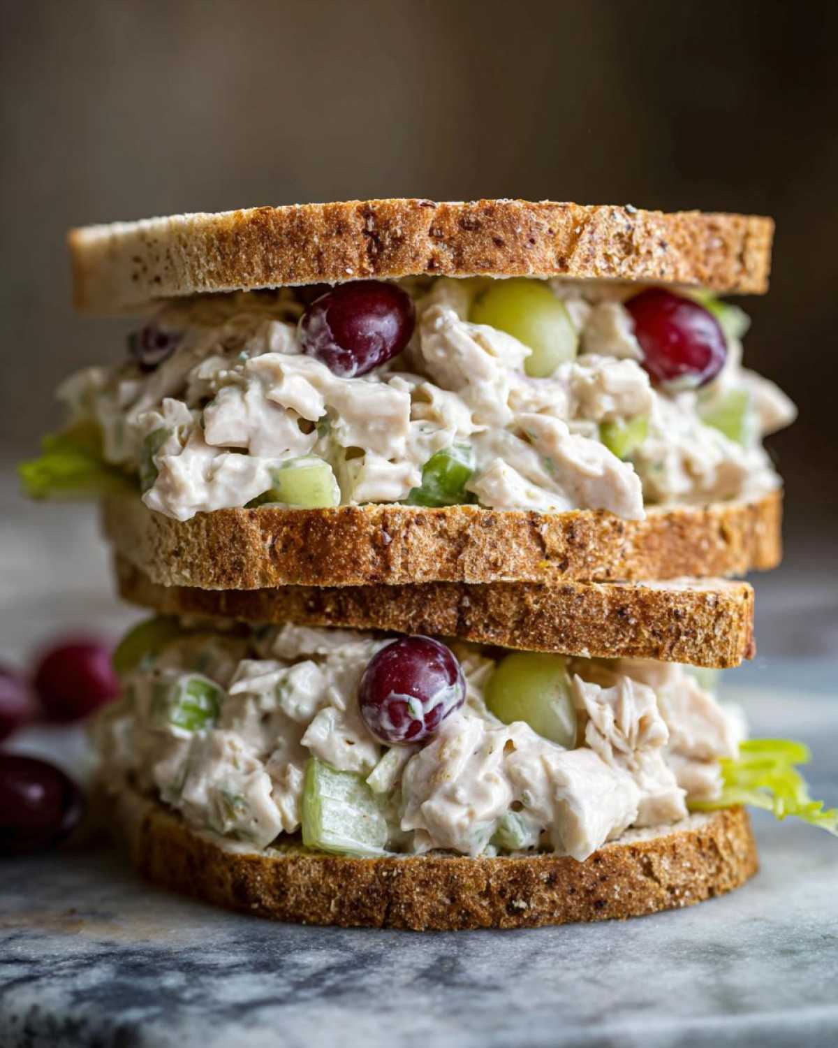 A tall, stacked chicken salad sandwich made with creamy filling, celery, red and green grapes, served between two slices of whole wheat bread.