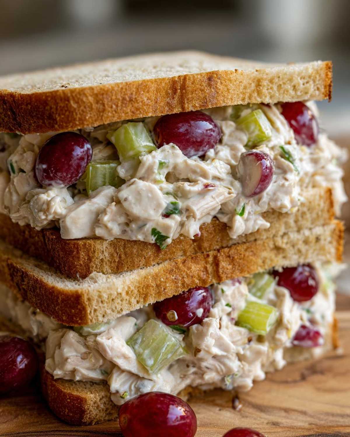 A tall, stacked chicken salad sandwich featuring creamy filling, celery, red grapes, and toasted bread.