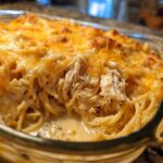 Close-up of creamy chicken spaghetti baked in a glass dish, showing shredded chicken and melted cheddar cheese.