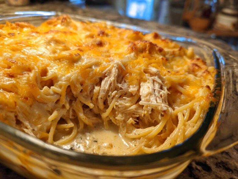 Close-up of creamy chicken spaghetti baked in a glass dish, showing shredded chicken and melted cheddar cheese.