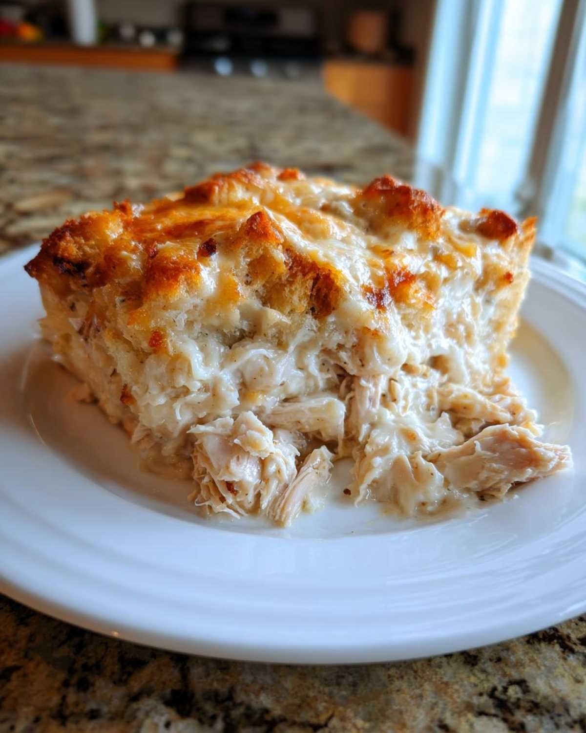 A square slice of creamy chicken stuffing casserole showing shredded chicken in a rich sauce and a golden, cheesy stuffing topping.