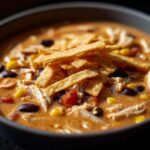 A close-up shot of a bowl filled with rich, creamy chicken tortilla soup topped with tortilla strips, black beans, and corn.