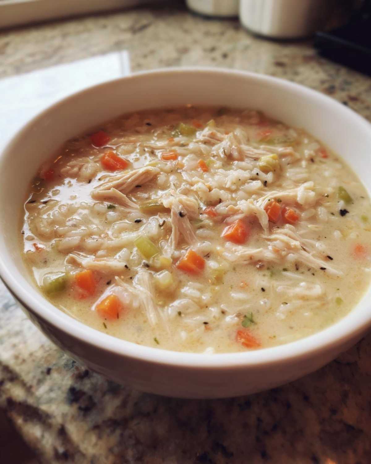 Close-up of a creamy chicken wild rice soup with visible shredded chicken, carrots, and celery in a white bowl.