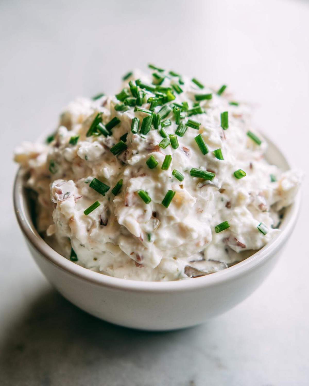 Close-up of creamy clam dip served in a white bowl, generously topped with freshly chopped green chives.