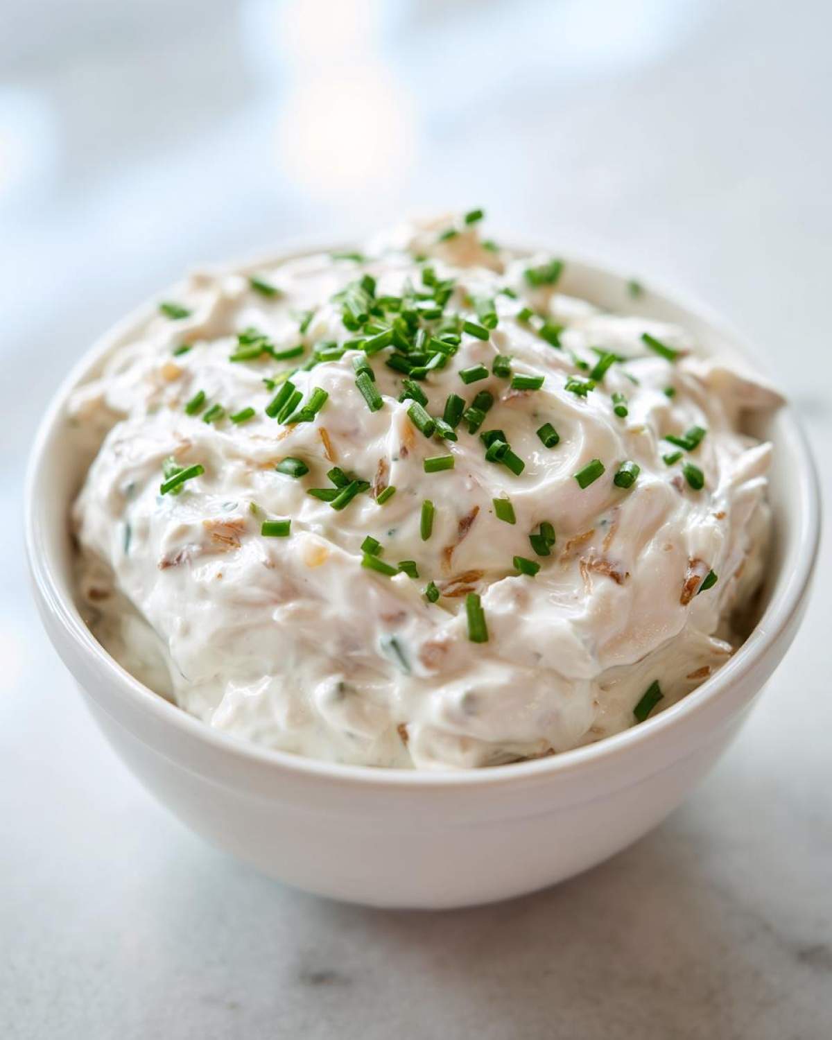 A white bowl filled with creamy clam dip, garnished generously with chopped green chives.