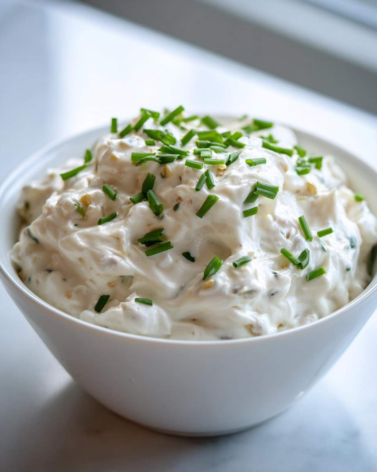 A white bowl filled with creamy clam dip, garnished generously with chopped fresh green chives.