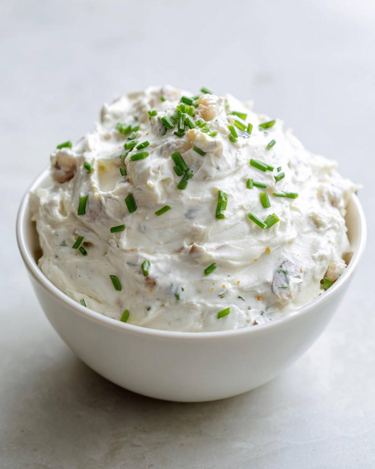 A white bowl filled with creamy clam dip, garnished generously with chopped fresh chives.