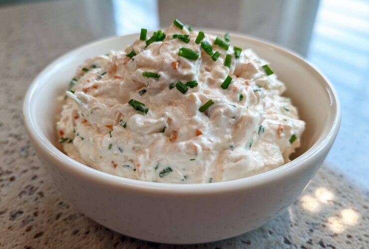 A close-up of creamy clam dip served in a white bowl, garnished generously with chopped green chives.