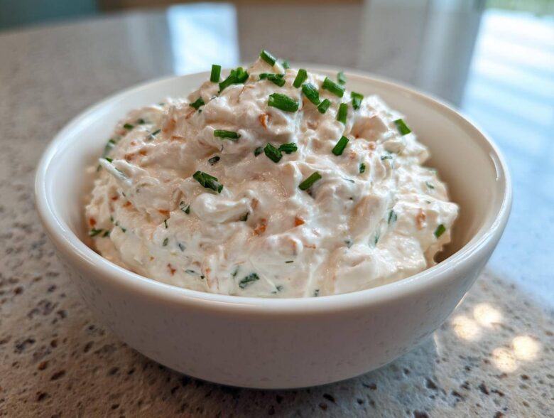 A close-up of creamy clam dip served in a white bowl, garnished generously with chopped green chives.