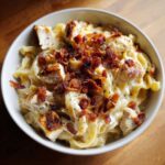 A close-up of a bowl of creamy Crack chicken pasta topped generously with crispy bacon bits and black pepper.