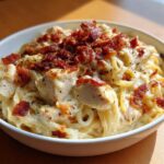 A close-up of a bowl of creamy Crack chicken pasta loaded with chunks of chicken and crispy bacon bits.