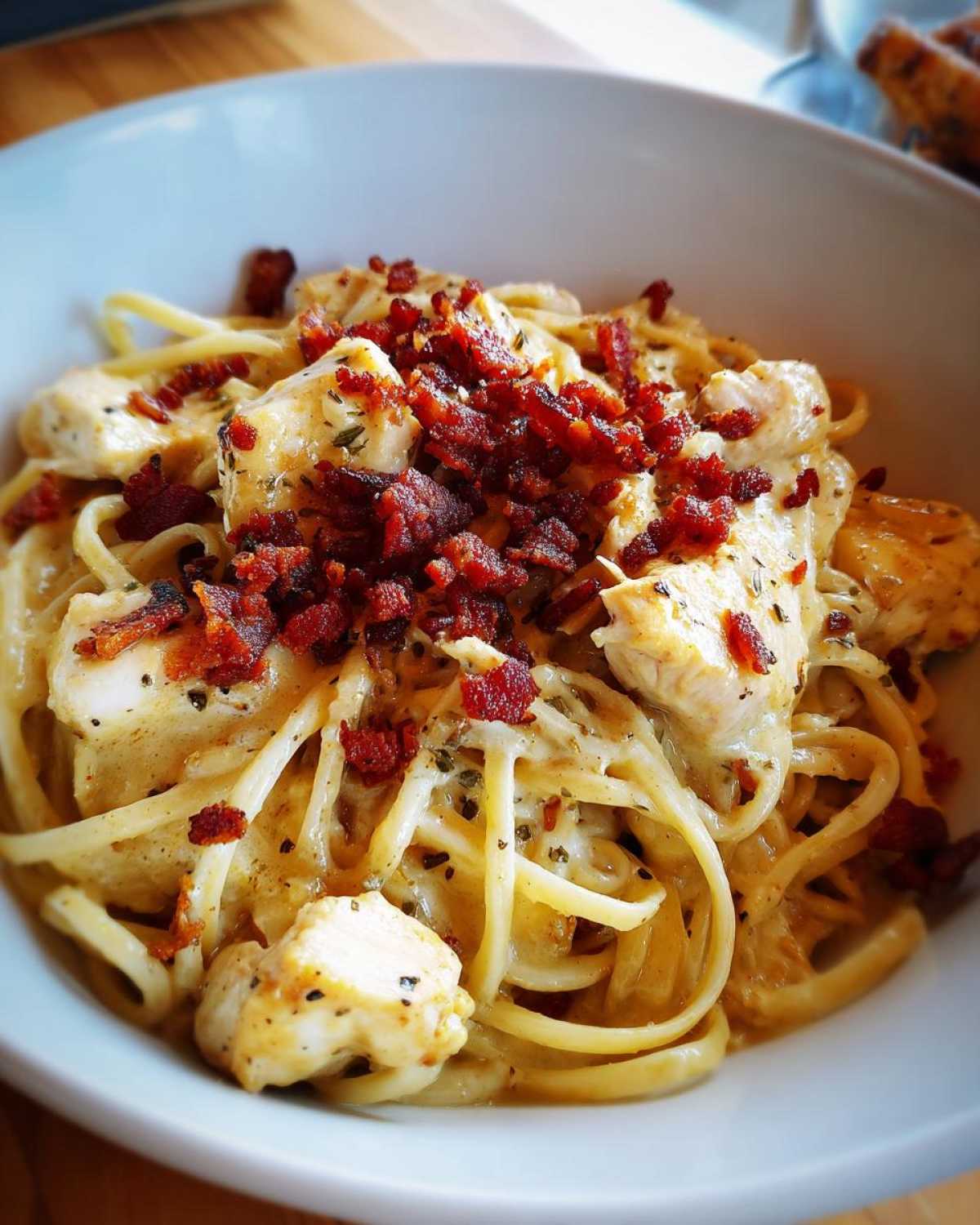 Close-up of a bowl of creamy Crack chicken pasta topped generously with crumbled bacon.