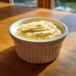 A close-up of thick, creamy garlic aioli served in a small white ramekin on a wooden surface.