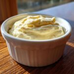 A close-up of creamy, pale yellow garlic aioli with visible specks of herbs in a small white ramekin.