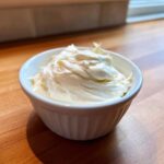 A small white ramekin filled with thick, creamy garlic sauce, sitting on a wooden countertop.