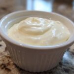 Close-up of thick, creamy garlic sauce served in a small white fluted ramekin on a granite countertop.