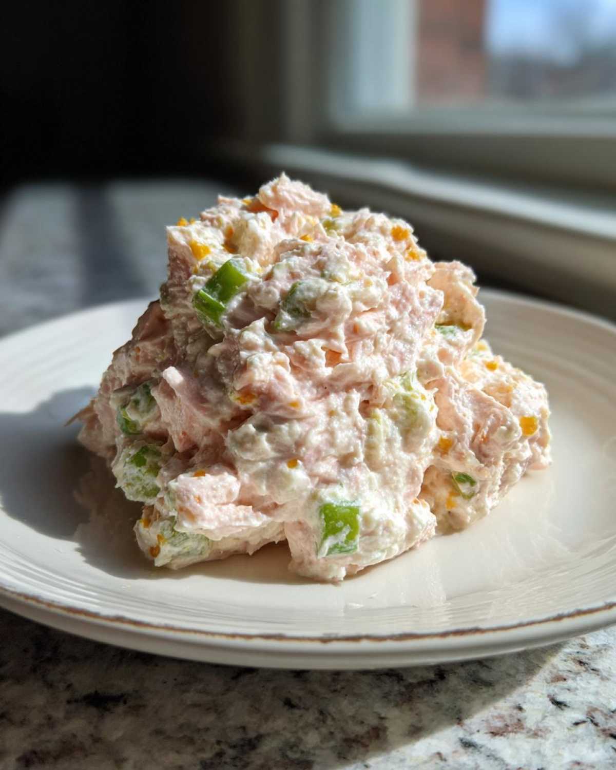 A mound of creamy ham salad mixed with green peppers and orange bits, served on a white plate.