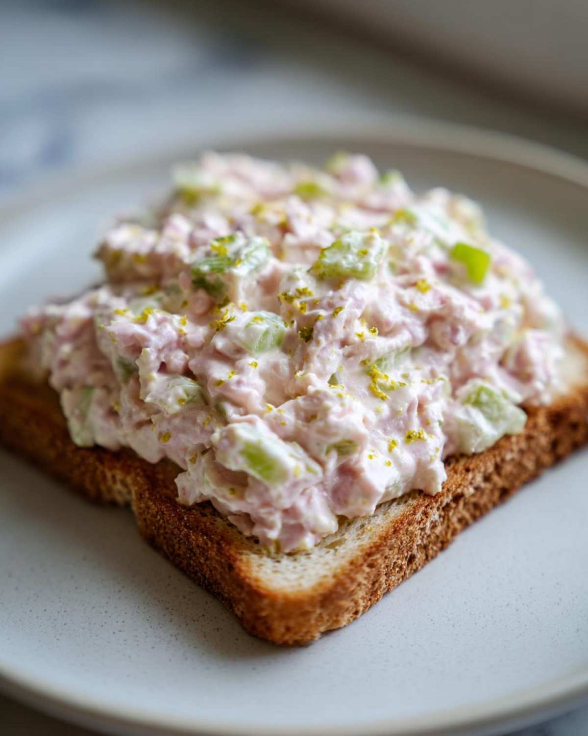 Close-up of creamy ham salad with celery and zest served on a piece of toasted bread.