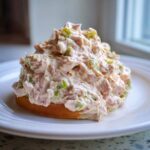 A generous mound of creamy ham salad with visible chunks of ham, celery, and mustard seeds served on a slice of toasted bread.