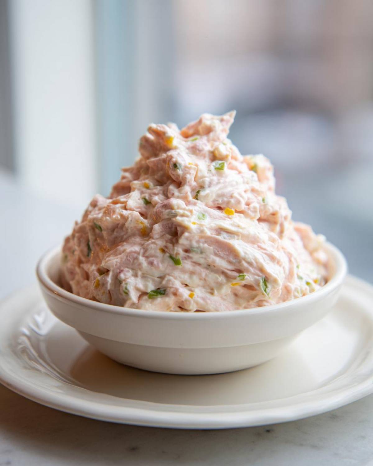 A generous mound of creamy ham salad mixed with green onions and yellow relish served in a white bowl.