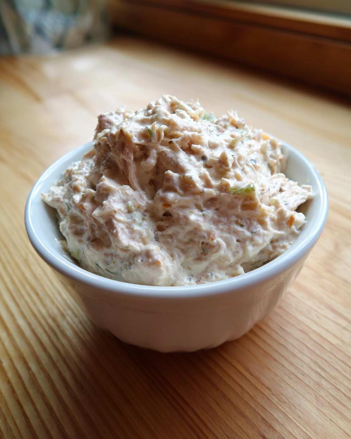 A close-up of a generous serving of creamy tuna dip piled high in a small white bowl on a wooden surface.