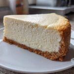 A perfect slice of creamy white chocolate cheesecake with a thick graham cracker crust, served on a white plate.