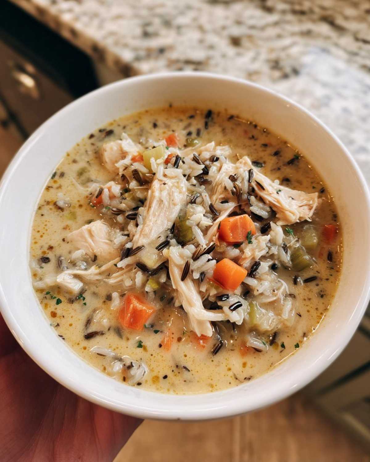A close-up of a creamy bowl of amazing wild rice soup, featuring shredded chicken, carrots, and celery.