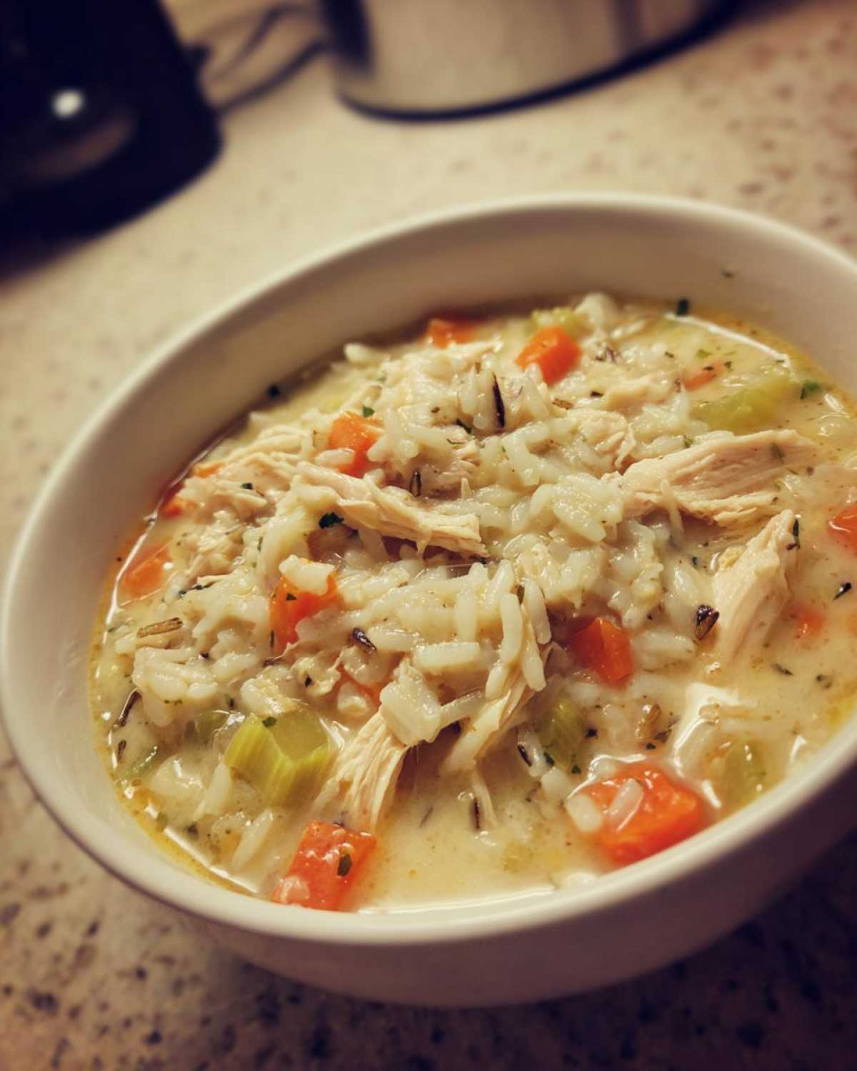 Close-up of a creamy chicken and wild rice soup filled with shredded chicken, carrots, and celery in a white bowl.