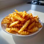 A mound of perfectly golden, crispy crinkle cut air fryer french fries piled high on a white plate.