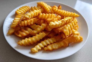 A close-up of golden brown, crispy crinkle cut air fryer french fries piled high on a white plate.