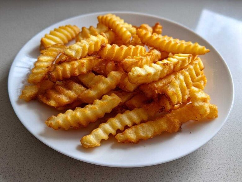A close-up of golden brown, crispy crinkle cut air fryer french fries piled high on a white plate.