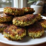 A stack of golden brown, crispy baked zucchini fritters piled high on a white plate.