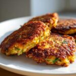 Close-up of four golden-brown, crispy Cabbage Fritters stacked slightly on a white plate.