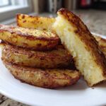 Close-up of perfectly crispy, golden brown potato wedges stacked on a white plate.