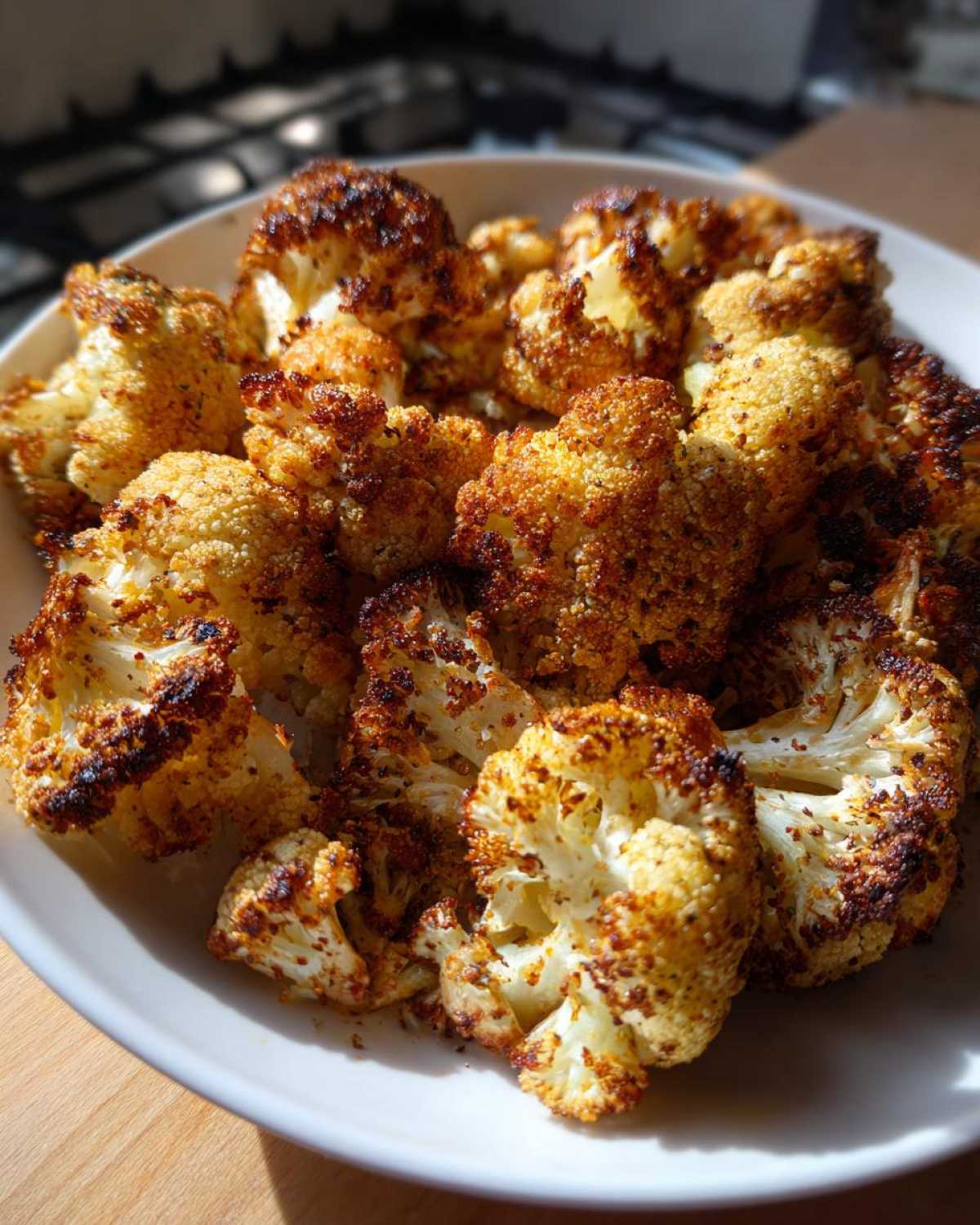 A close-up of golden brown and deeply caramelized crispy roasted cauliflower florets served in a white bowl.