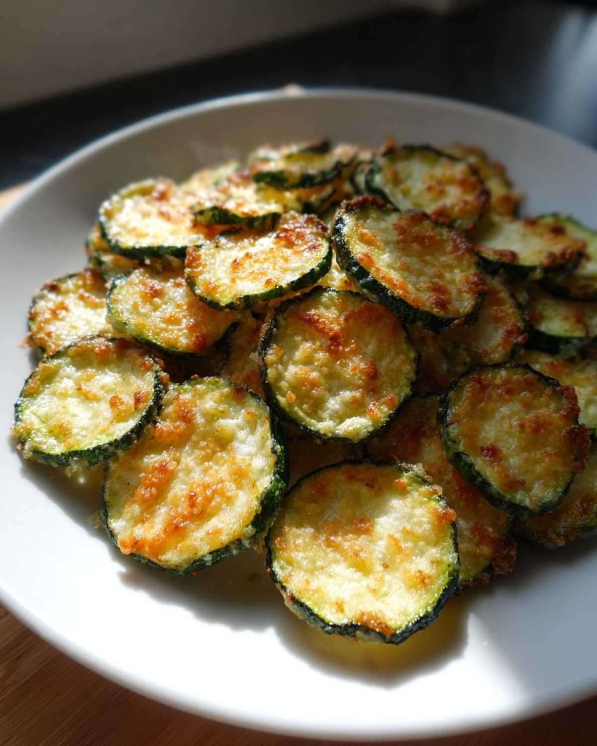 A plate piled high with crispy zucchini chips topped with melted, browned cheese.