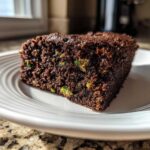 Close-up of a moist slice of Crowd Favorite Chocolate Zucchini Sheet Cake showing green zucchini pieces.