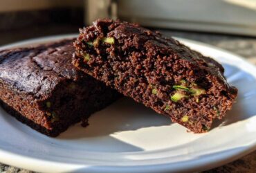 Two slices of moist Crowd Favorite Chocolate Zucchini Sheet Cake showing visible green zucchini shreds in the rich chocolate crumb.
