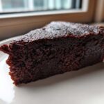 Close-up of a rich, dark slice of decadent fudgy avocado brownies on a white plate.