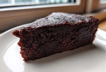 Close-up of a rich, dark slice of decadent fudgy avocado brownies on a white plate.