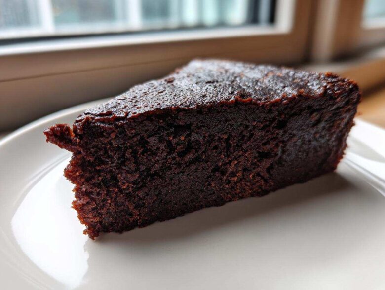 Close-up of a rich, dark slice of decadent fudgy avocado brownies on a white plate.