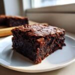 A close-up of a rich, dark square of decadent fudgy avocado brownies on a white plate.