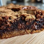 A close-up of a decadent fudgy brookie bar showing the chewy cookie top and the rich, molten chocolate brownie layer with melted chips.