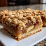Close-up of a thick slice of delicious & easy apple pie bars featuring a buttery crust, gooey apple filling, and a crunchy crumble topping.