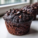 Close-up of a rich, dark Double Chocolate Zucchini Muffin topped generously with chocolate chips.