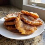 A stack of freshly fried, golden brown buñuelos generously coated in cinnamon sugar on a white plate.