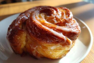 Close-up of a golden brown, freshly baked honey bun with thick white glaze, part of a homemade honey bun recipe.